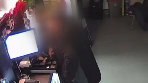 Ystradgynlais RFC A man, whose image is blurred so he is not identifiable, is seen putting his hand into an open till.