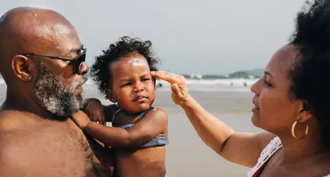 Getty Images Woman putting sunscreen on small child's face on a beach