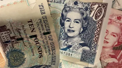 Three paper notes. The one on the right has writing on it which says 'The States of Guernsey' with 'Ten Pounds' written underneath. The second note has a picture of Queen Elizabeth II with a '10' in the top left corner and a red note underneath with the same picture. 