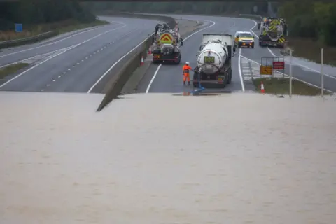 Reuters A man and several maintenance vehicles pumping out flood water from the A421 in Bedfordshire