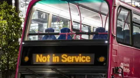 PA Media The top floor of a pink double decker bus sits empty. The illuminated sign at the front of the bus says 'not in service'.