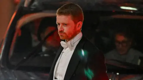 Reuters A man in a black dinner suit with a white shirt and bowtie. He has short hair and is sat in front of a taxi.