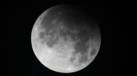 The moon during a partial lunar eclipse. A shadow is covering part of the moon's top half.