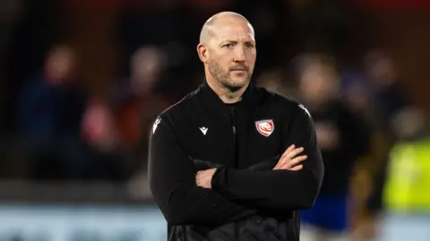 Gloucester director of rugby George Skivington stands wearing a black team polo jumper with his arms folded across his chest