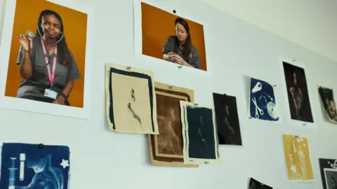 Pictures part of the NHS Darkroom project pinned to a wall using pins. They include images of staff and images similar to radiographies or bodies and objects.