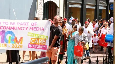 A crowd of people stand behind a banner, which has the words Inclusion, care, integrity