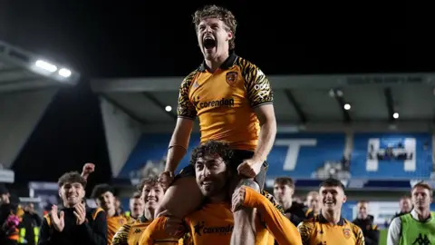 Hull City's Regan Slater, wearing the amber and black kit, is carried on the shoulders of a team-mate at the final whistle after the Championship play-off semi-final second leg match at The Den in London