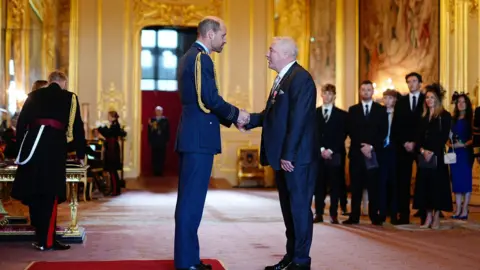 PA Media Ally McCoist shaking hands with Prince William, as his family observe in the background