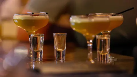 PA Media Three cocktail glasses with three shot glasses on a blurred table.