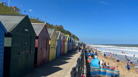 A row of colourful beach huts on a path above a beach on a sunny day at Mundesley, Norfolk