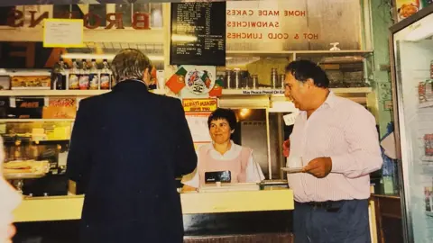 Freitas family Filomena and Agostinho Freitas behind the counter in Brown's in the 1990s and serving a man in a suit.