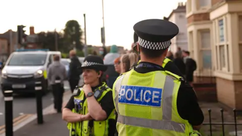 PA Media Two police officers stand on a street's pavement 