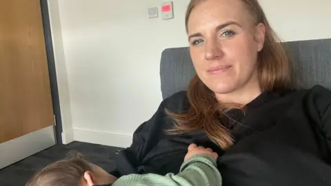 Redcar and Cleveland Borough Council Lauren Somerville. She has long brown hair and is wearing a black top. She is sitting on a chair and her young son is on her knee.