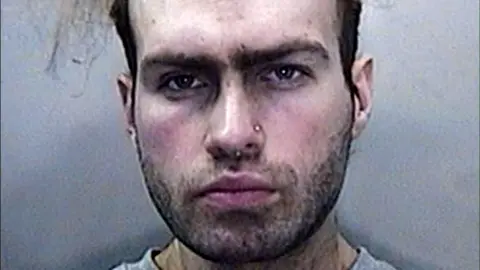 South Wales Police South Wales Police 'mugshot' of Luke Deeley aft  his arrest, looking unshaven with a chemoreceptor  ringing  and hairsbreadth  shaved astatine  the sides