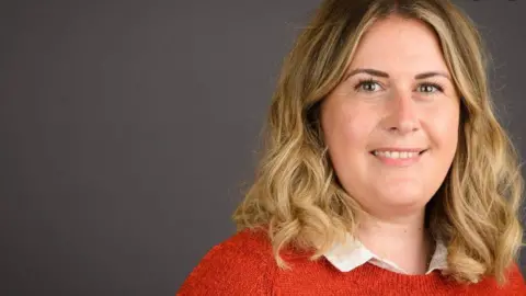 BCP Council Woman looking at the camera smiling, she has shoulder length blonde wavy hair and brown eyes and a orange knitted jumper.