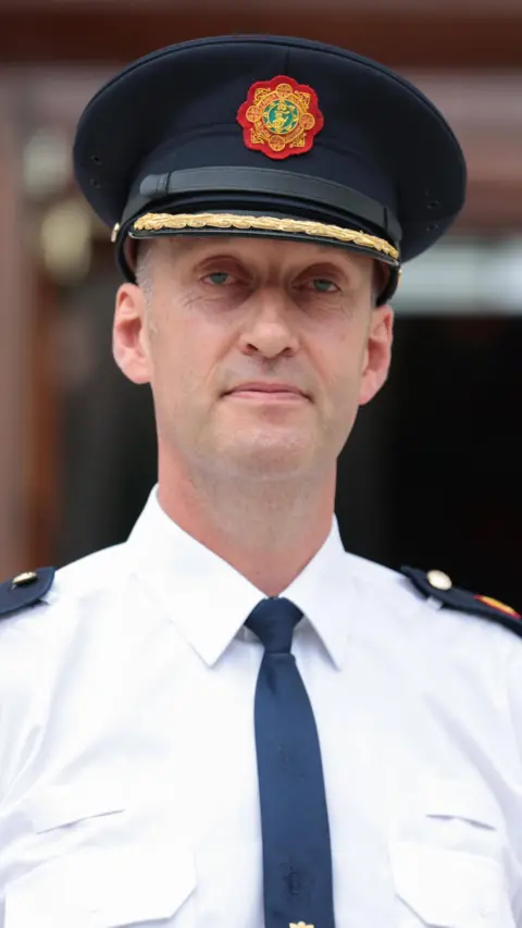Garda commissioner in a black officer hat, white shirt and black tie. 