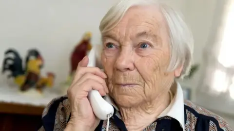 An older woman holding a telephone