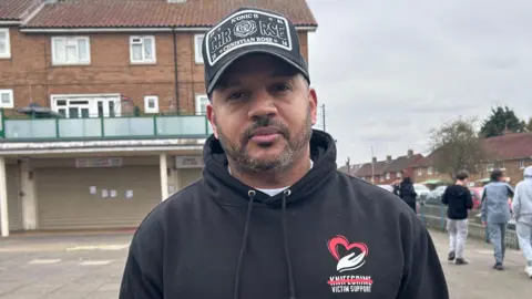 Kate Bradbrook/BBC Quinton Green a man standing outside wearing a black hoodie and black baseball cap.