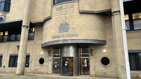 The exterior of Bradford Crown Court - a beige brick building with silver revolving doors.
