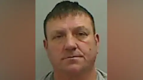 Mugshot of Pearce. He is white, clean shaven, of a stocky build and has short brown hair.