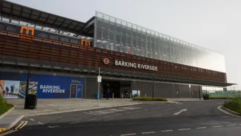 A new train station with a large glass and frontage. There is a train standing on the elevated platform. 