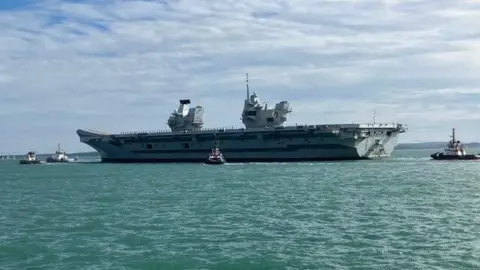 The large carrier at sea next to tug boats