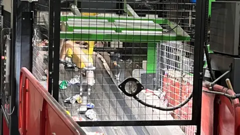 A yellow arm in a cage hangs over a converyor belt 