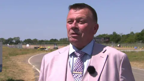 A man with short brown hair in a pink suit and tie.