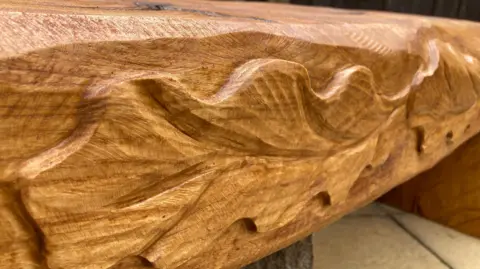 A wooden bench with oak leaves carved into it.