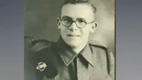 Roy Hayward A black and white photo of Roy Hayward in military uniform wearing glasses and looking at the camera.