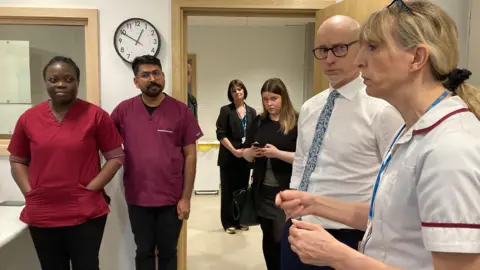 A man wearing a white shirt and blue tie, surrounded by medics. 