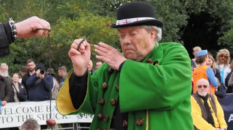 The World Conker Championships David Jakins is dressed successful  greenish  and adorned with conkers. He is focusing connected  a crippled  of conkers helium  is presently  playing.