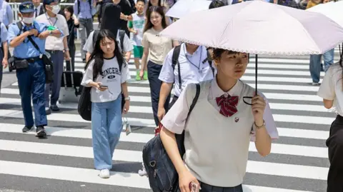 Japanese school girl with an umbrella walks over a crossroad on a summer day