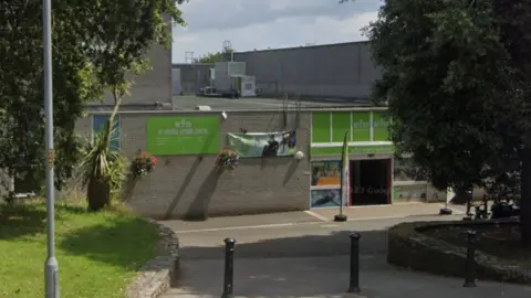 A grey building which says St Austell Leisure Centre on a green sign. There are green trees on either side. 