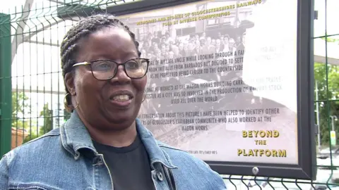 Hazel Golden wearing glasses and a denim jacket standing in front of a billboard for Beyond the Platform.