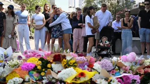 Reuters Crowds gather by floral tributes to victims of the Bondi mall stabbings
