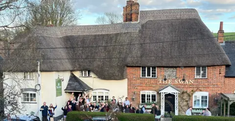 Sophie Cooper People stood outside a pub smiling and waving at the camera