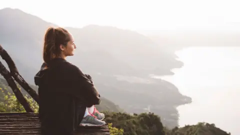 A young woman sits on an elevated platform overlooking the coastline.