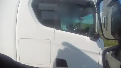 A white lorry being filmed driving on the M5, by a driver who police said is rolling a cigarette without his hands on the wheel