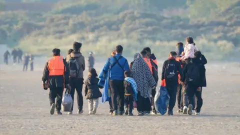 A group of people, some wearing life jackets, walking along a beach