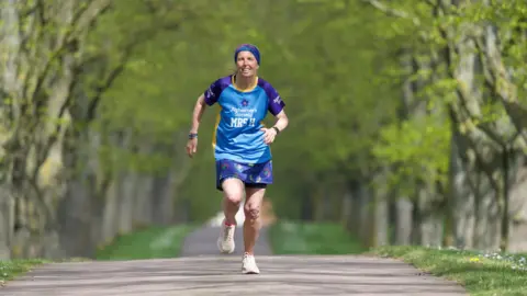 John Fairhall/BBC Apryl running in a blue and purple vest, with pink shoes and blue headband through the trees in training