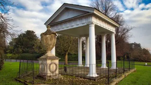 A white temple-like structure with a large urn beside it.