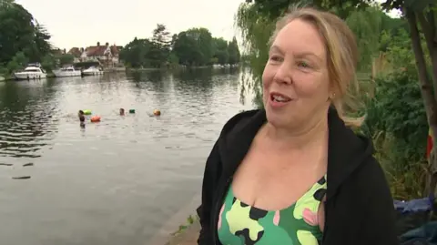 Marlene Lawrence, founder of swimming group, the Teddington Bluetits, being interviewed by the BBC while standing next to the River Thames