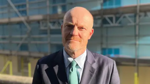 A man wearing a suit and tie standing in front of a scaffolded building.