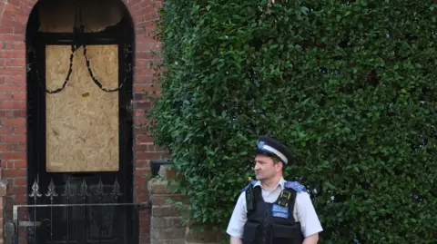 Reuters A police officer standing in front of a door, boarded up with a wooden board