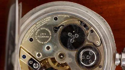 Mallams The inside of the Paul Ditisheim deck watch. It has gold coloured mechanisms.