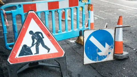 Getty Images Under construction board sign on the closed road with arrow sign and traffic cone. Caution symbol under construction, work in progress sign. - stock photo