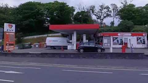 The exterior of the petrol station, a red shelter, which has a sign that reads EVF, there is a small shop to one side.