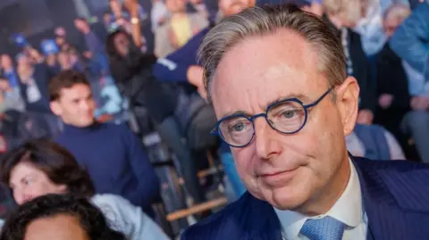 EPA/Shutterstock Belgium's prime minister Bart de Wever wearing blue glasses and a blue suit in front of a crowd