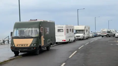 A row of motorhomes and cars parked on a Saltburn seafront on a grey day.